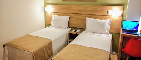 Een hotelkamer met twee bedden, een bureau met een laptop, een rode stoel en een schilderij van een landschap aan de muur.
