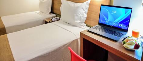 Une chambre d’hôtel avec deux lits, un ordinateur portable sur un bureau et une assiette de fruits.