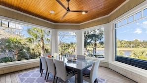 A covered patio with a glass table, wicker chairs, and a ceiling fan. - Pristine getaway with tranquil views (Kiawah Island)