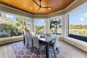 A covered patio with a glass table, wicker chairs, and a ceiling fan.