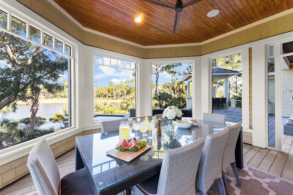 A sunlit dining area with a table set for four, large windows, and a view of a lake.