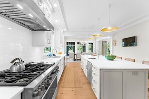 A modern kitchen with white cabinetry, a central island, stainless steel appliances, and pendant lighting.