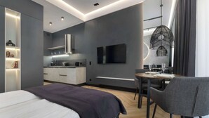 Habitación de hotel moderna con cama, mesa de comedor, televisor y cocina.