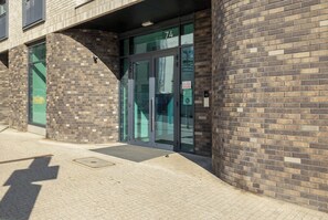 A building entrance with glass doors, a number '74' above the entrance, and a brick facade.