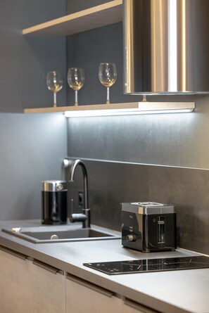 A modern kitchen with a stainless steel range hood, a coffee maker, a toaster, and a sink.