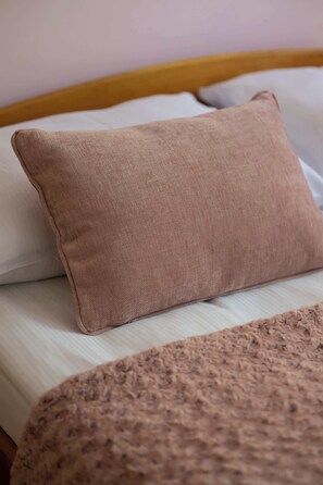 Una cama con una almohada color beige y una manta texturizada.