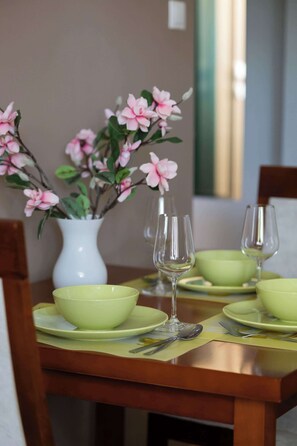 Una mesa de comedor con platos verdes, fuentes y un jarrón con flores rosas.