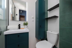 Un baño moderno con un lavamanos blanco, gabinetes verde agua y un inodoro blanco.