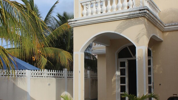 A two-story building with a swimming pool, potted plants, and a white fence.