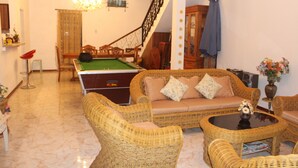 A living room with a pool table, wicker furniture, a staircase, and a chandelier.