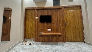 A room with a wooden wardrobe, a mounted television, and a small shelf with remote controls.