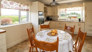 A kitchen with white cabinets, a dining table with chairs, and a view of the outdoors through the windows. - Dunbrody Dreams (Campile)