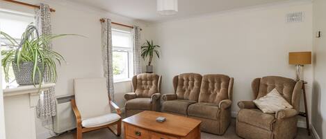 A living room with a wooden coffee table, two armchairs, a sofa, a white radiator, a ceiling fan, and a potted plant.
