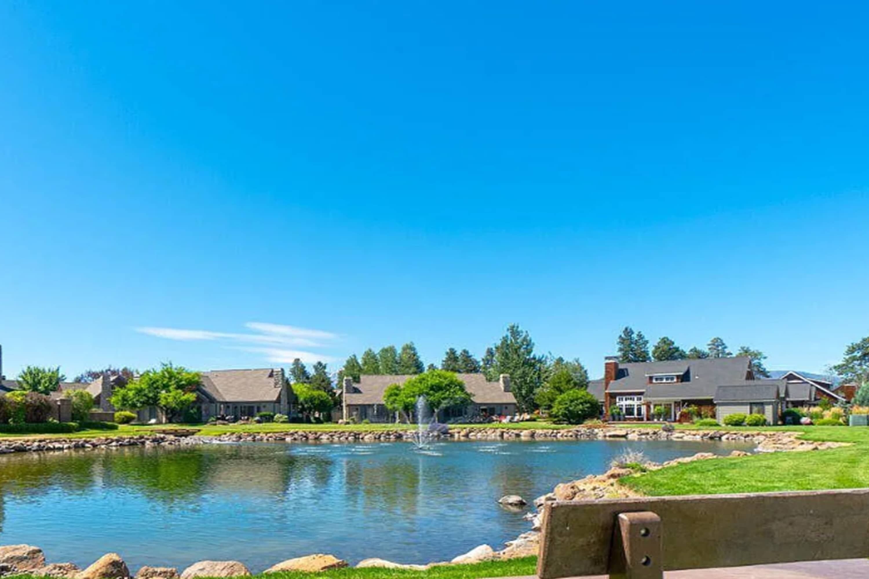 A residential area with a pond, houses, and a clear sky.