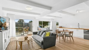 A modern, open-plan living space with a sofa, dining table, and kitchen area. - Werri Heights - great family home including your pet (Gerringong)