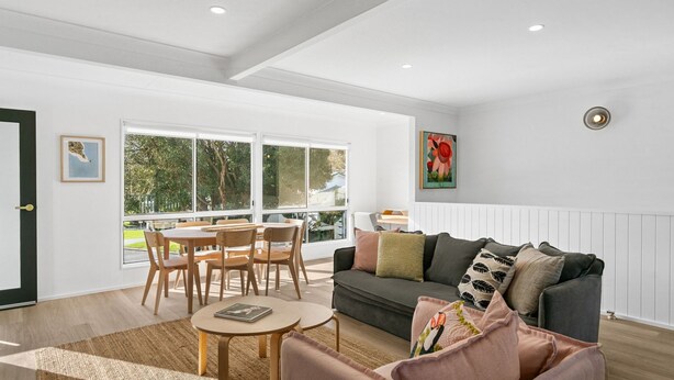 A spacious living area with a dining table, chairs, a sofa, and a large window offering a view of the outdoors. - Werri Heights - great family home including your pet (Gerringong)