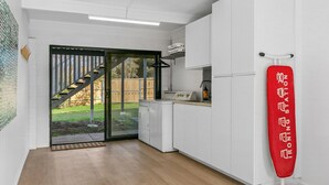 A modern kitchen with white cabinets, a built-in oven, and a red ironing board. - Werri Heights - great family home including your pet (Gerringong)