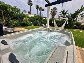 A hot tub with a waterfall feature, surrounded by lush greenery and palm trees. - Stylish Garden Villa • Hot Tub • Fireplace • Wi-Fi (Carvoeiro)