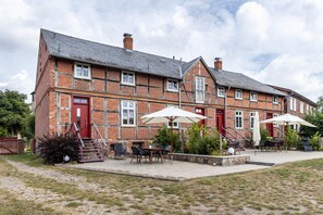 A brick building with a red door, outdoor seating area with tables and chairs, and a staircase leading to the entrance. - Apartment '1' with Private Terrace, Shared Garden and Wi-Fi (Groß Pankow)