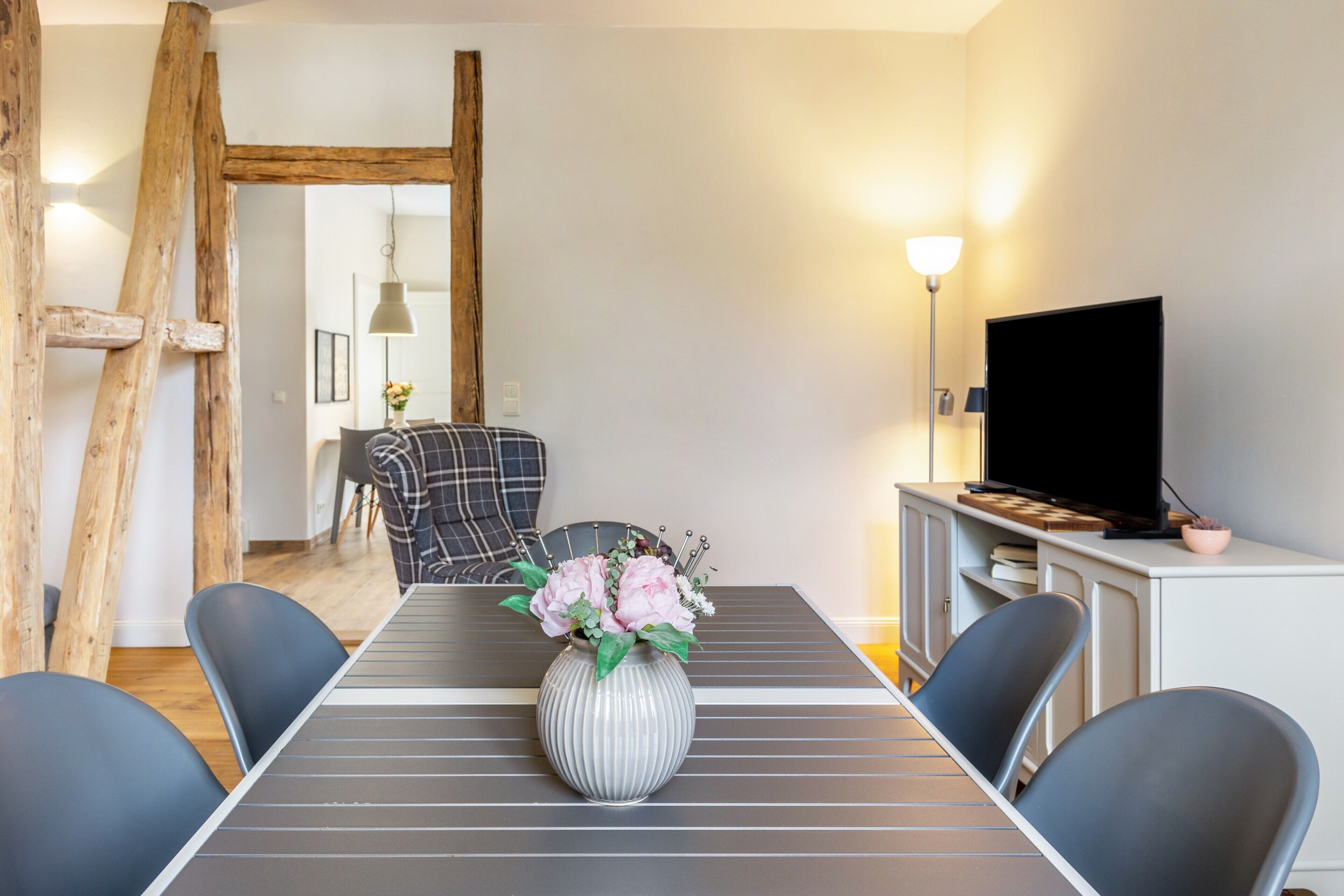 A dining area with a table, chairs, a vase with flowers, a television, and a lamp.