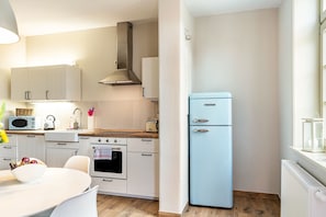 A modern kitchen with white cabinets, a blue refrigerator, a stove, and a dining area with a table and chairs.