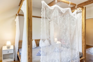 A bedroom with a canopy bed, a nightstand, a lamp, and a wooden headboard.