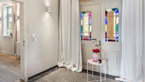 Een hal met een witte deur, een klein tafeltje met een vaas en een beker, en een radiator.