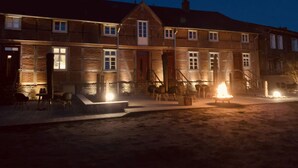 A two-story building with a central entrance, a fire pit in the foreground, and a paved area in front. - Apartment '4 Putlitz' with Private Terrace, Shared Garden and Wi-Fi (Groß Pankow)