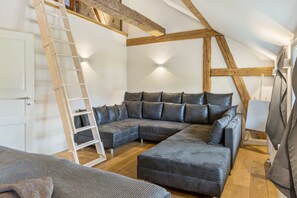 A loft-style room with a wooden ceiling, a sectional sofa, a ladder, and a laptop on a table.