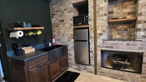 Una cocina con pared de ladrillo, armarios de madera, microondas empotrado y estufa a leña.