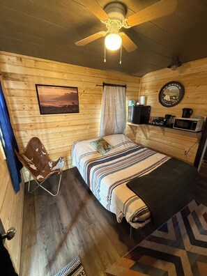 A cozy room with a bed, a chair, a ceiling fan, a picture on the wall, and a coffee station. - Chief Lone Walker #6 (East Glacier Park)