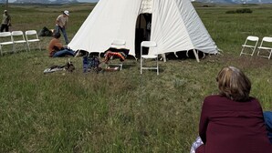 A white teepee with a ladder, surrounded by white chairs in a grassy field. - Chief Lone Walker #6 (East Glacier Park)