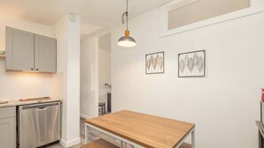 A modern kitchen with a dishwasher, a wooden table, and a bench. There are two framed artworks on the wall.