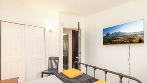 A bedroom with a bed, a chair, a TV mounted on the wall, and a door leading to another room.