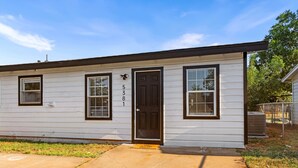 A single-story white house with a dark brown door, numbered 5381, and two windows with dark frames.