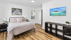 A bedroom with a bed, bedside tables, a nightstand, a dresser, a window, and two wall-mounted paintings.