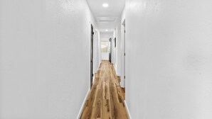 A narrow hallway with white walls and wooden flooring, leading to a door at the end.