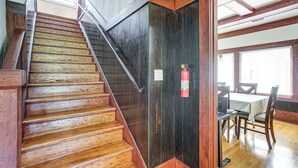 Una escalera de madera con barandilla de metal, un extintor de incendios montado en la pared y un comedor con mesa y sillas.