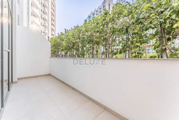 Un balcon doté d’un mur blanc et d’un sol carrelé, d’où l’on peut admirer une rangée d’arbres et d’immeubles.