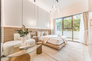 Une chambre d’hôtel moderne avec une table basse en verre, un canapé, un lit avec une tête de lit en bois et une grande fenêtre donnant sur un paysage verdoyant.