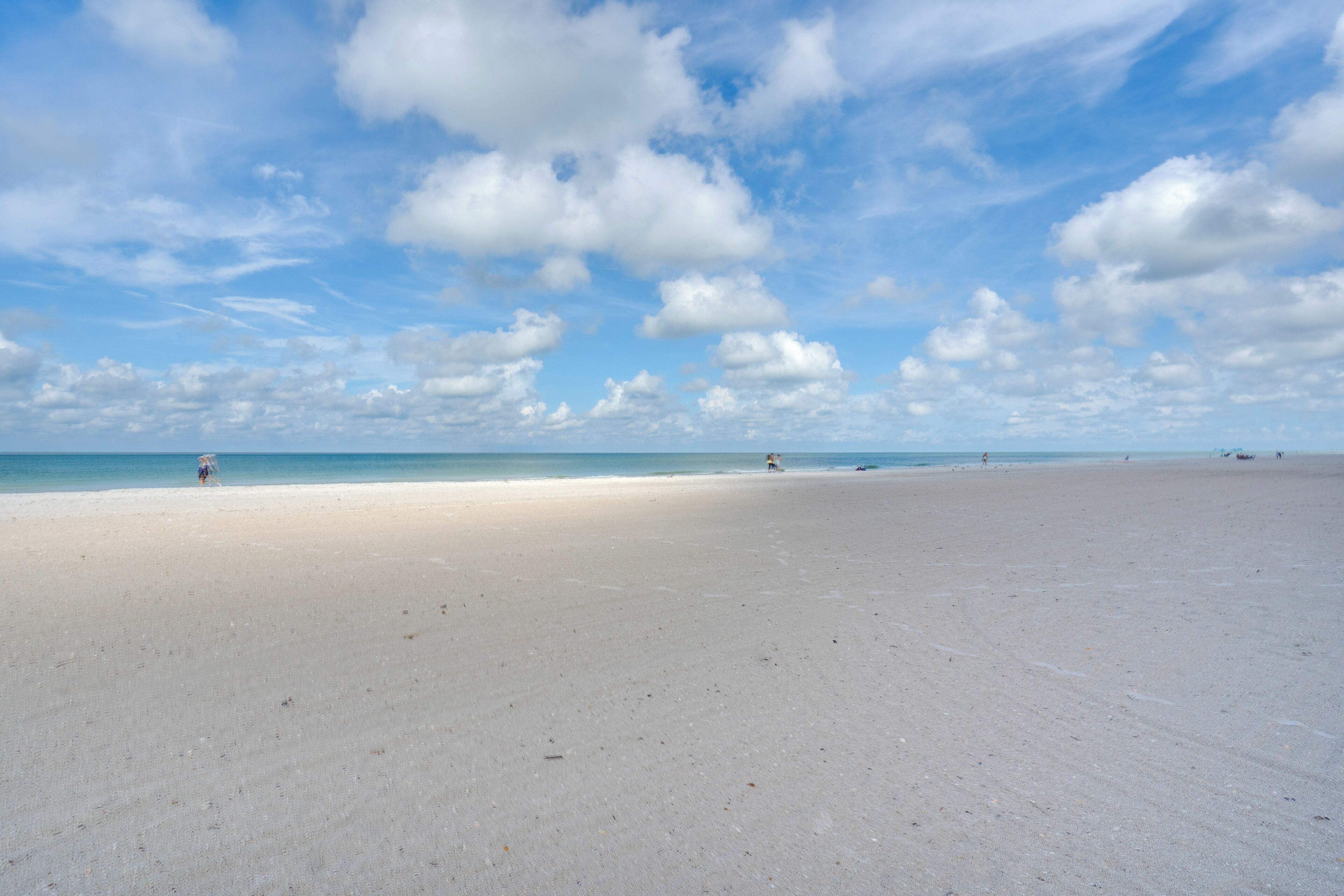 A wide, sandy beach with a clear sky and scattered clouds.