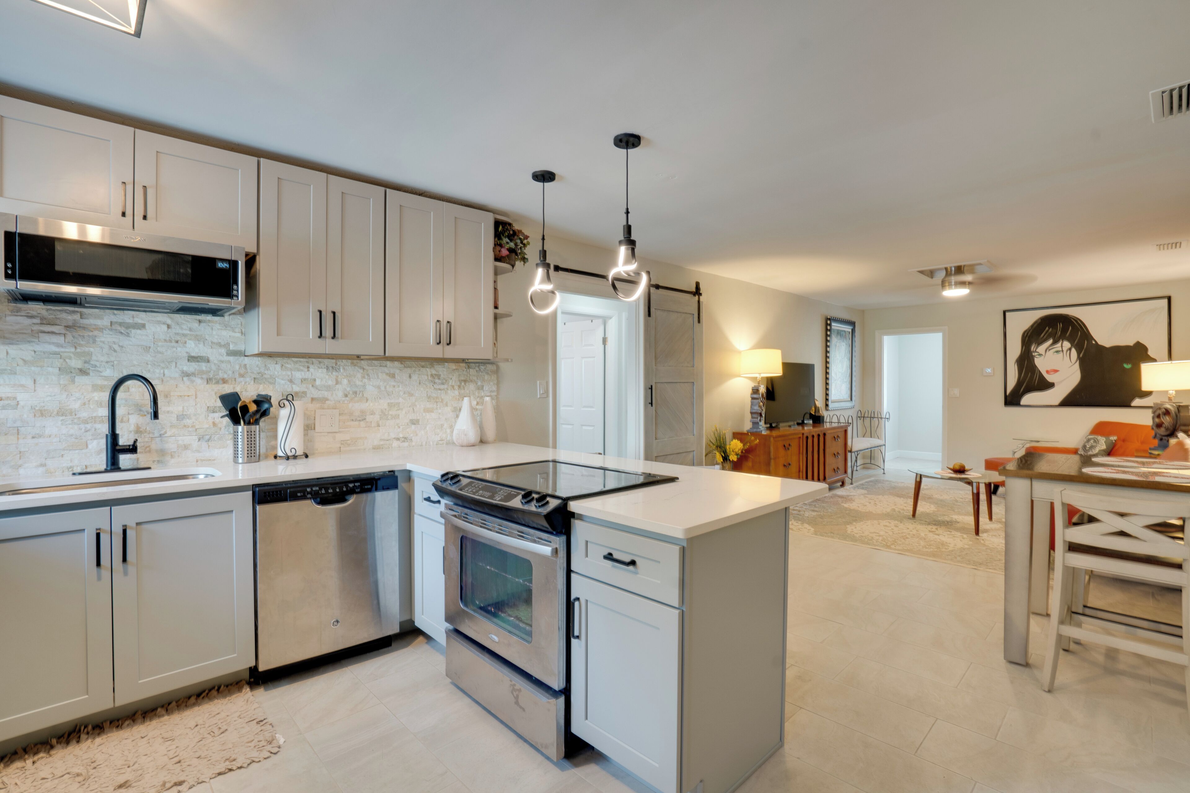 A modern kitchen with stainless steel appliances, white cabinetry, and pendant lighting.