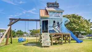 Un’area giochi a tema spiaggia con uno scivolo e una panchina di legno.