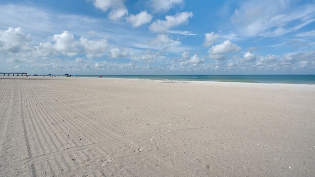 Ein weiter, sandiger Strand mit klarem Himmel und einer entfernten Küstenlinie.