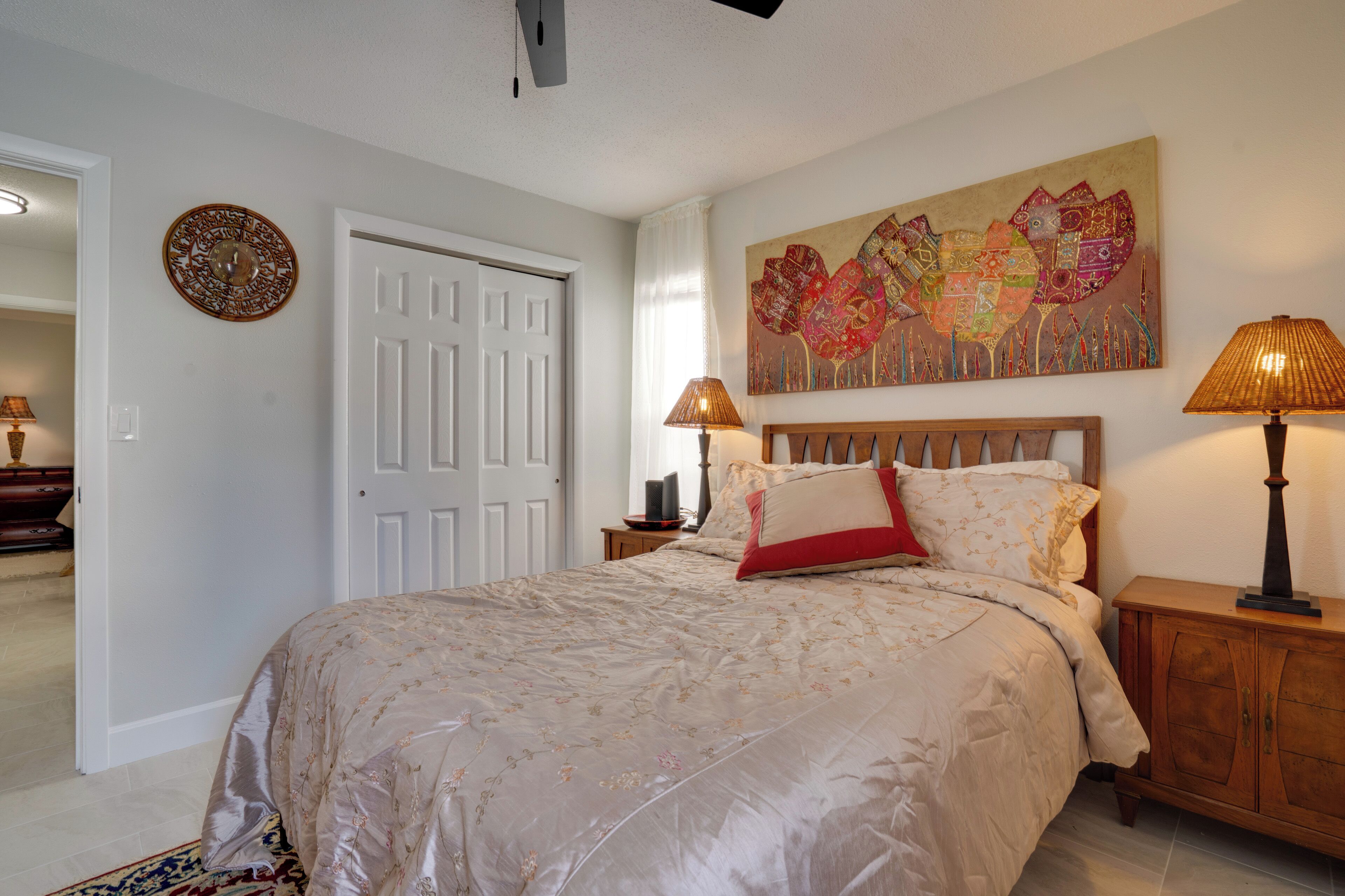 A bedroom with a large bed, two bedside lamps, a wooden nightstand, a decorative wall piece, and a door.