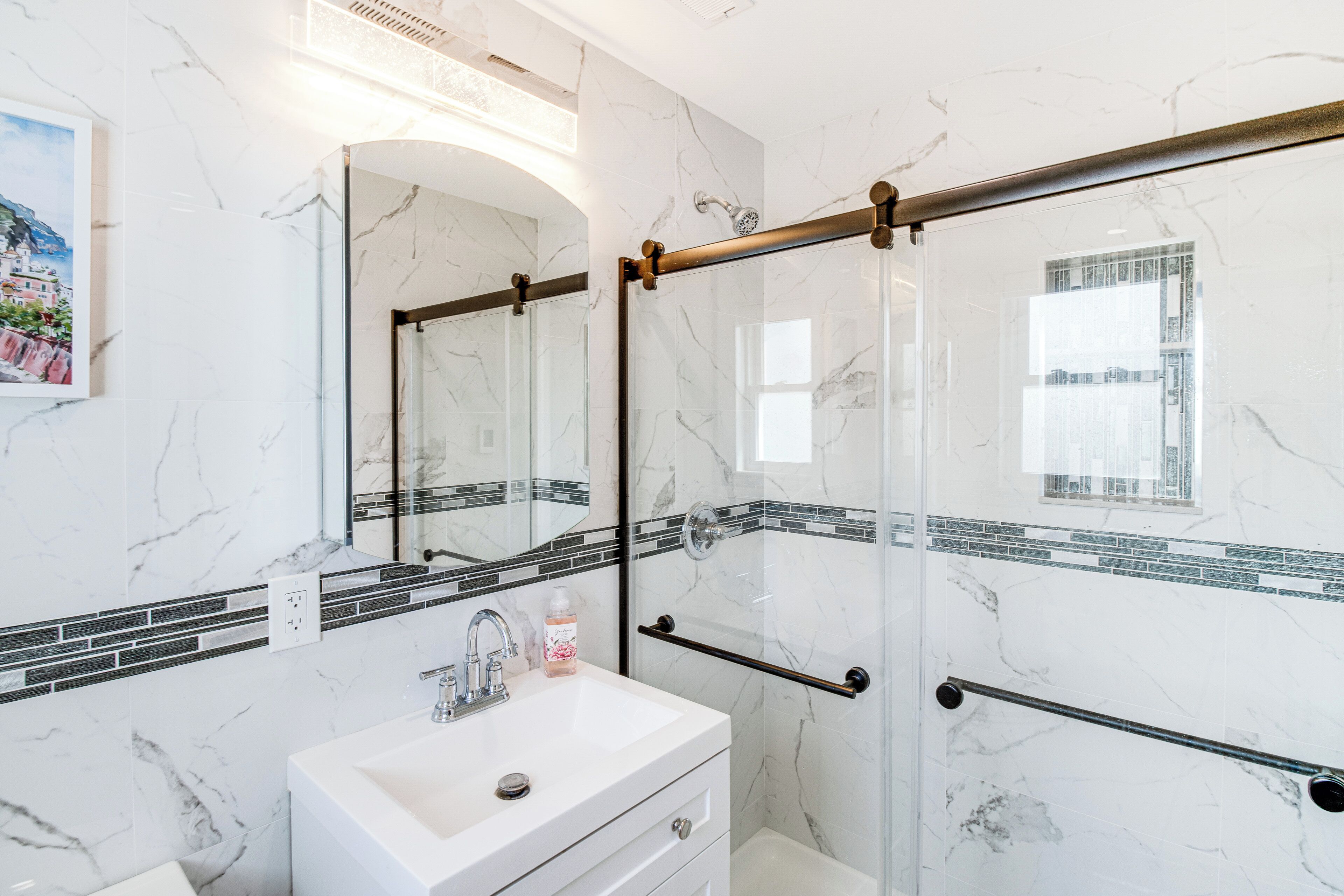 Une salle de bain avec un lavabo en marbre blanc, un grand miroir et une cabine de douche en verre.