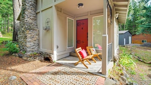 A house with a stone exterior, a red door, and a porch with two wooden chairs.