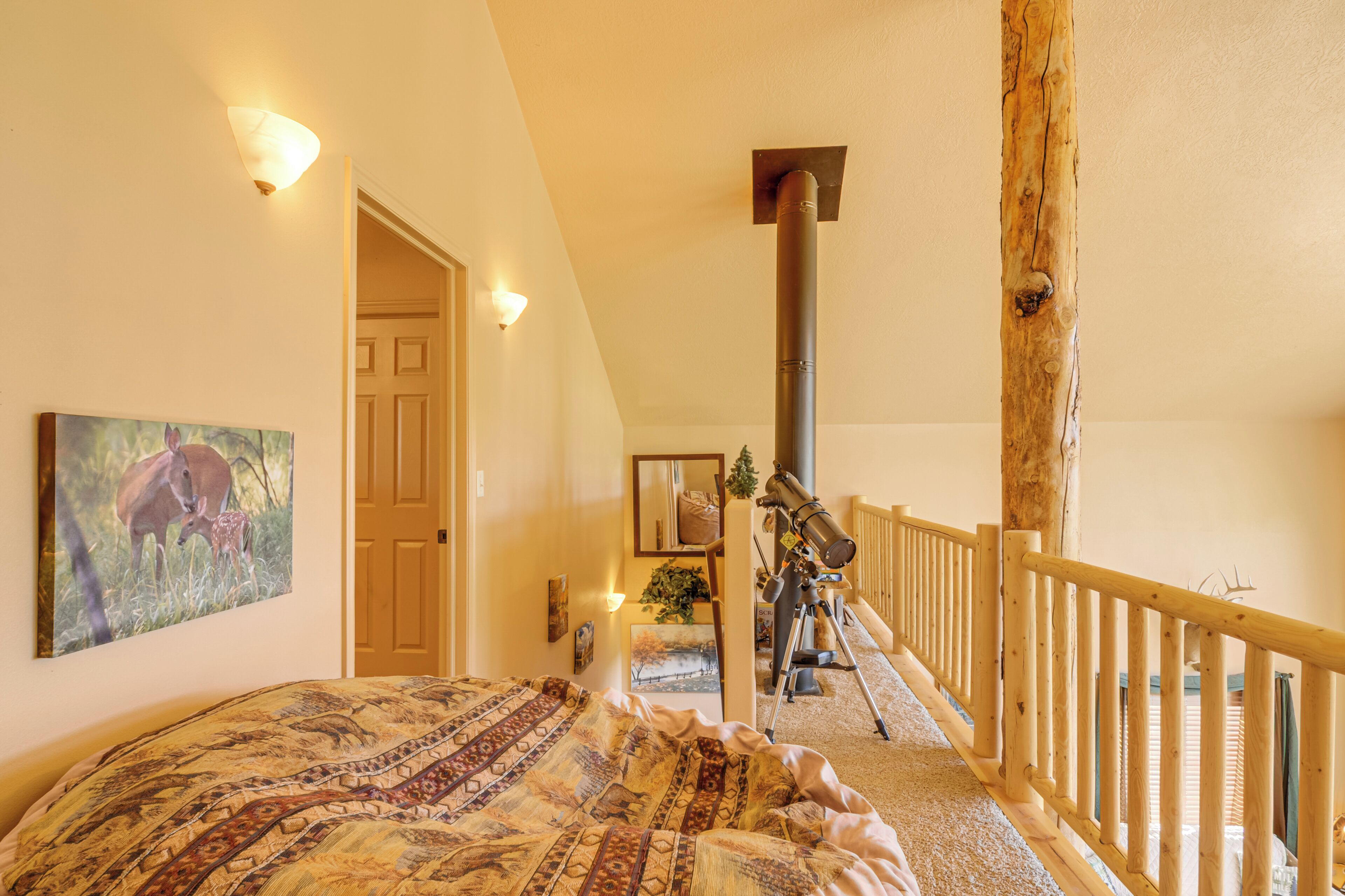 A bedroom with a large bed, a wooden railing, a telescope, and a door leading to another room.