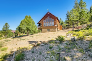 A wooden cabin with a balcony, surrounded by trees and a gravel path. - Luxe Cabin Retreat, Near Bryce & Zion Nat'l Parks! (Duck Creek Village)