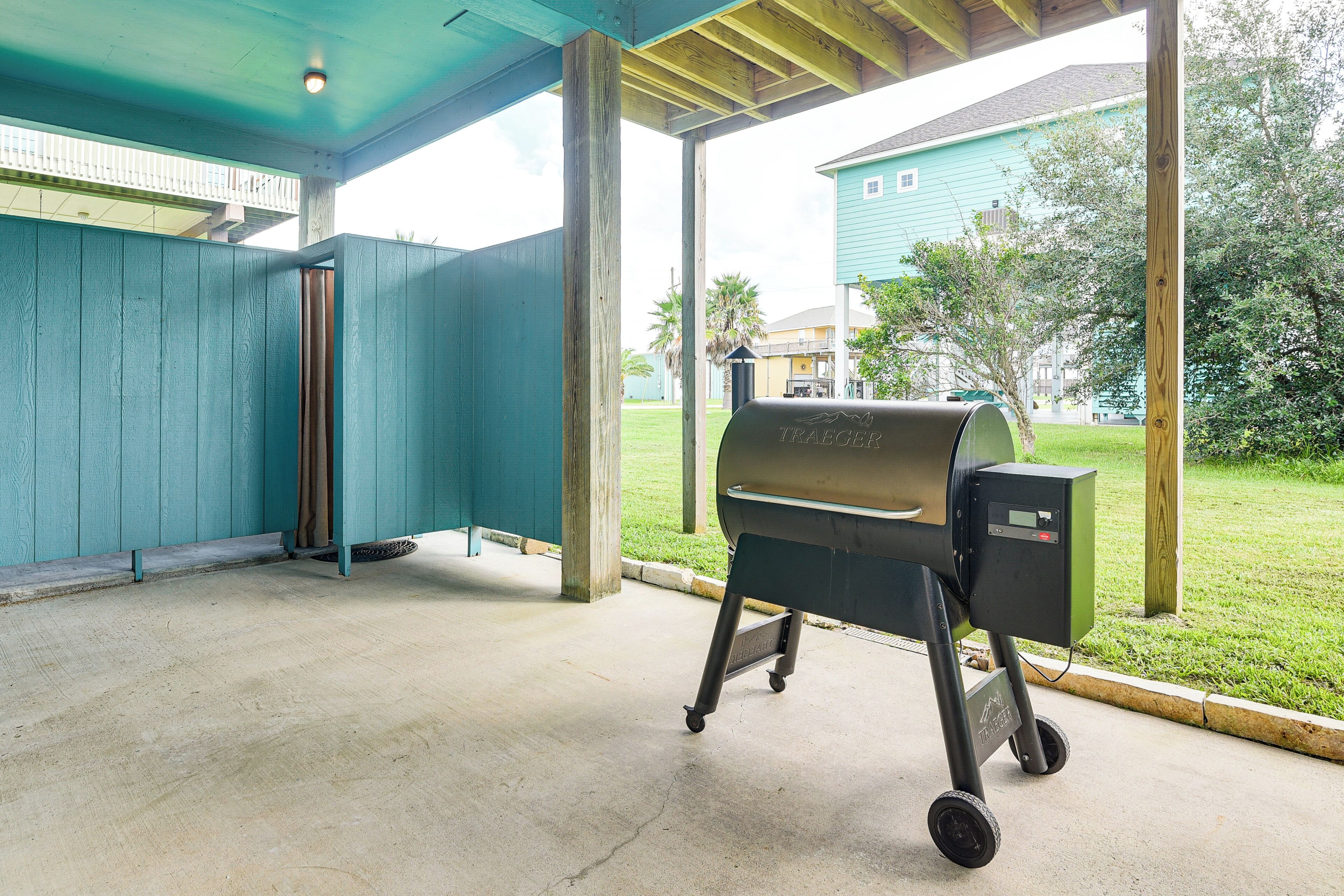 Patio esterno coperto con barbecue portatile, pavimento in cemento e vista su zona residenziale con case e vegetazione.